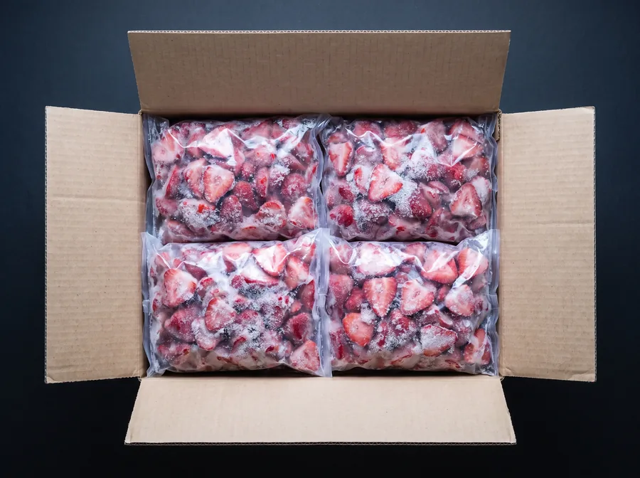 Caja de cartón abierta con cuatro bolsas de 2,5 kg de frutilla congelada
